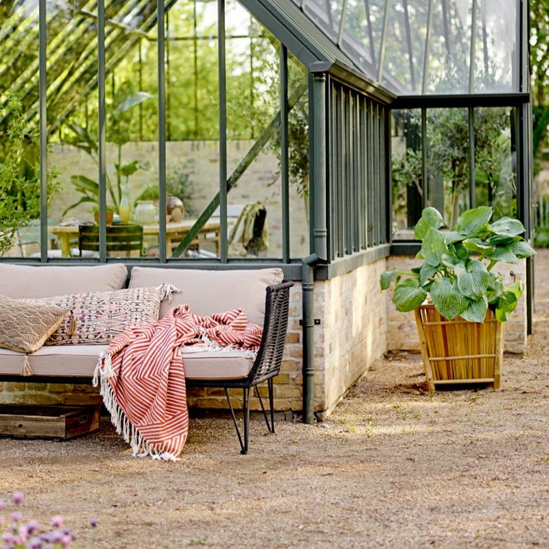 Gartensofa aus schwarzem Metall im Garten vor einem Greenhouse, ideal für entspannte Stunden im Freien.