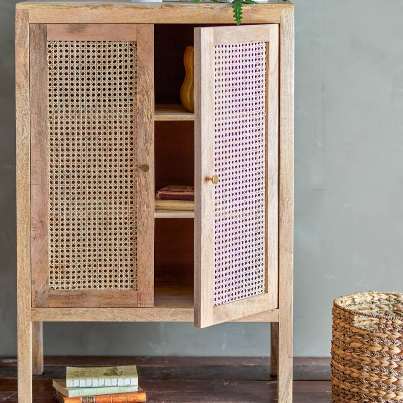 Schrank aus Mangoholz mit Rattan-Türen, 105 cm hoch, vor einer Wand, leicht geöffnet und gefüllt mit Büchern. 